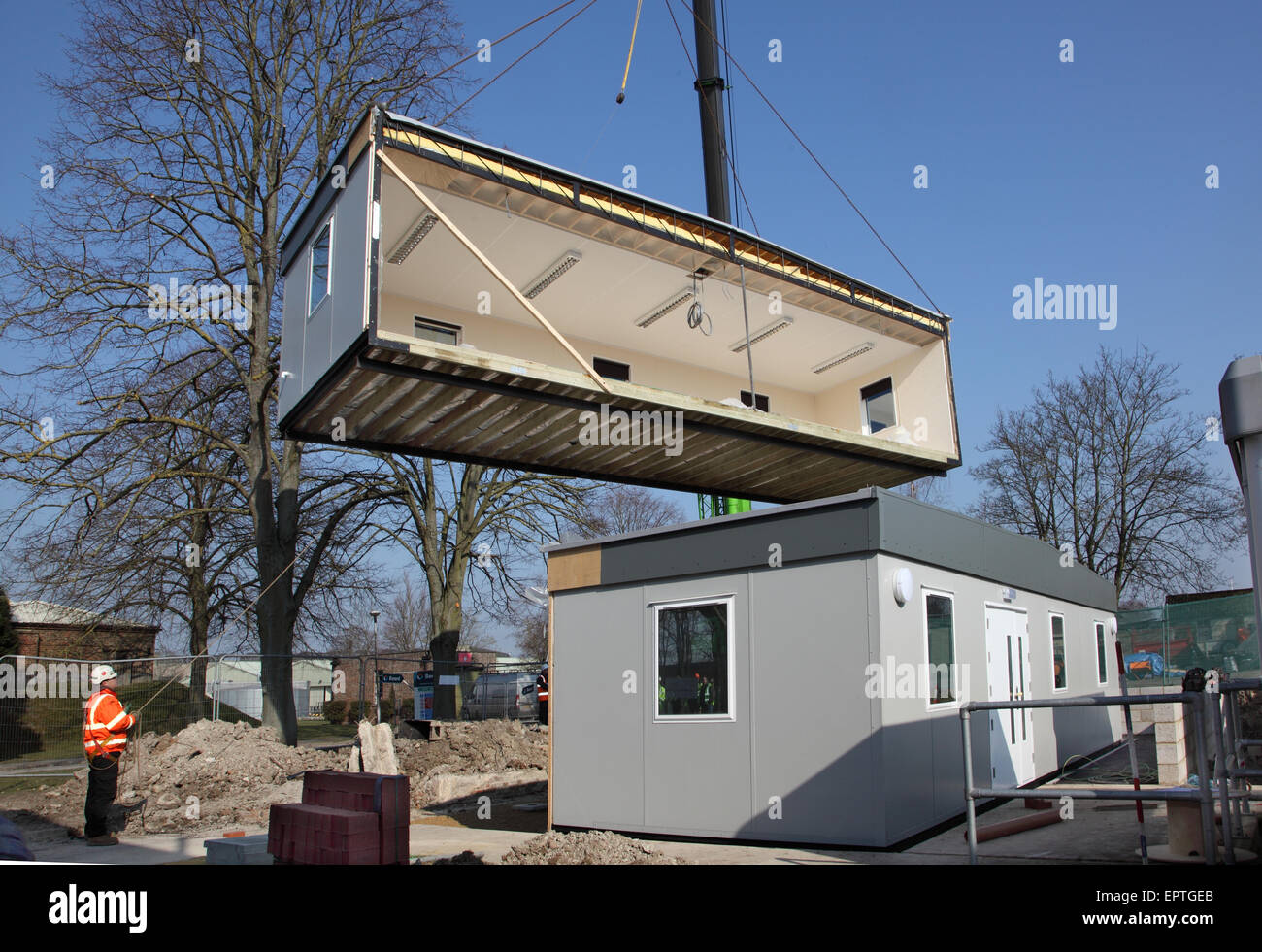 A section of a modular classroom building hangs from a crane during the installation of a new 2-section building. Stock Photo