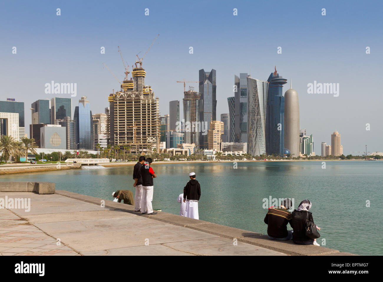 Young Qataris sit by the water with Doha skyscrapers in view Stock Photo