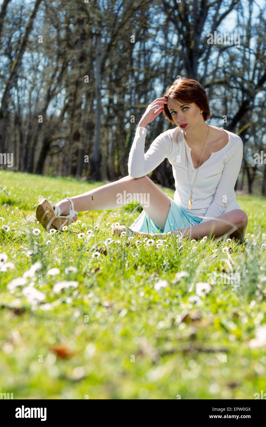 Beautiful woman sitting in the grass surrounded by spring daisies Stock Photo