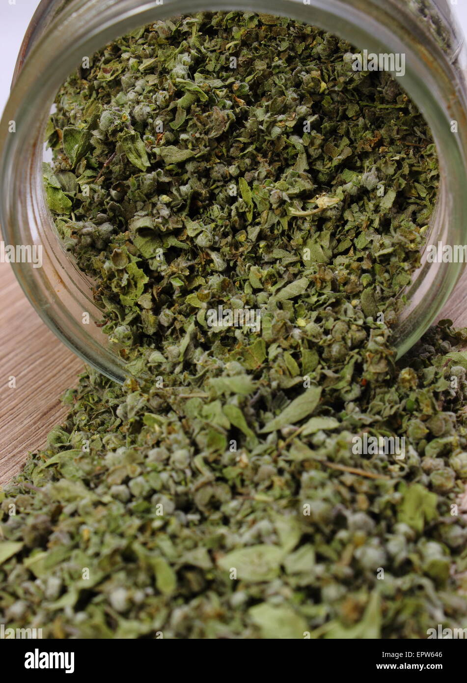 Heap of dried marjoram spilling out of glass jar on wooden background