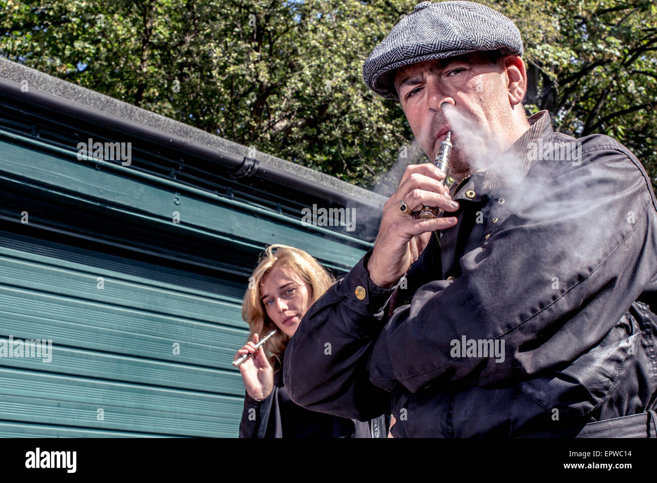 Man and woman standing smoking e-cigarettes outdoors with a lowe angle view off the middle-aged man exhaling smoke from his nost Stock Photo