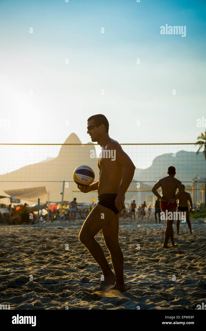 RIO DE JANEIRO, BRAZIL - FEBRUARY 01, 2014: Young carioca Brazilians play a sunset silhouette game of beach volleyball. Stock Photo