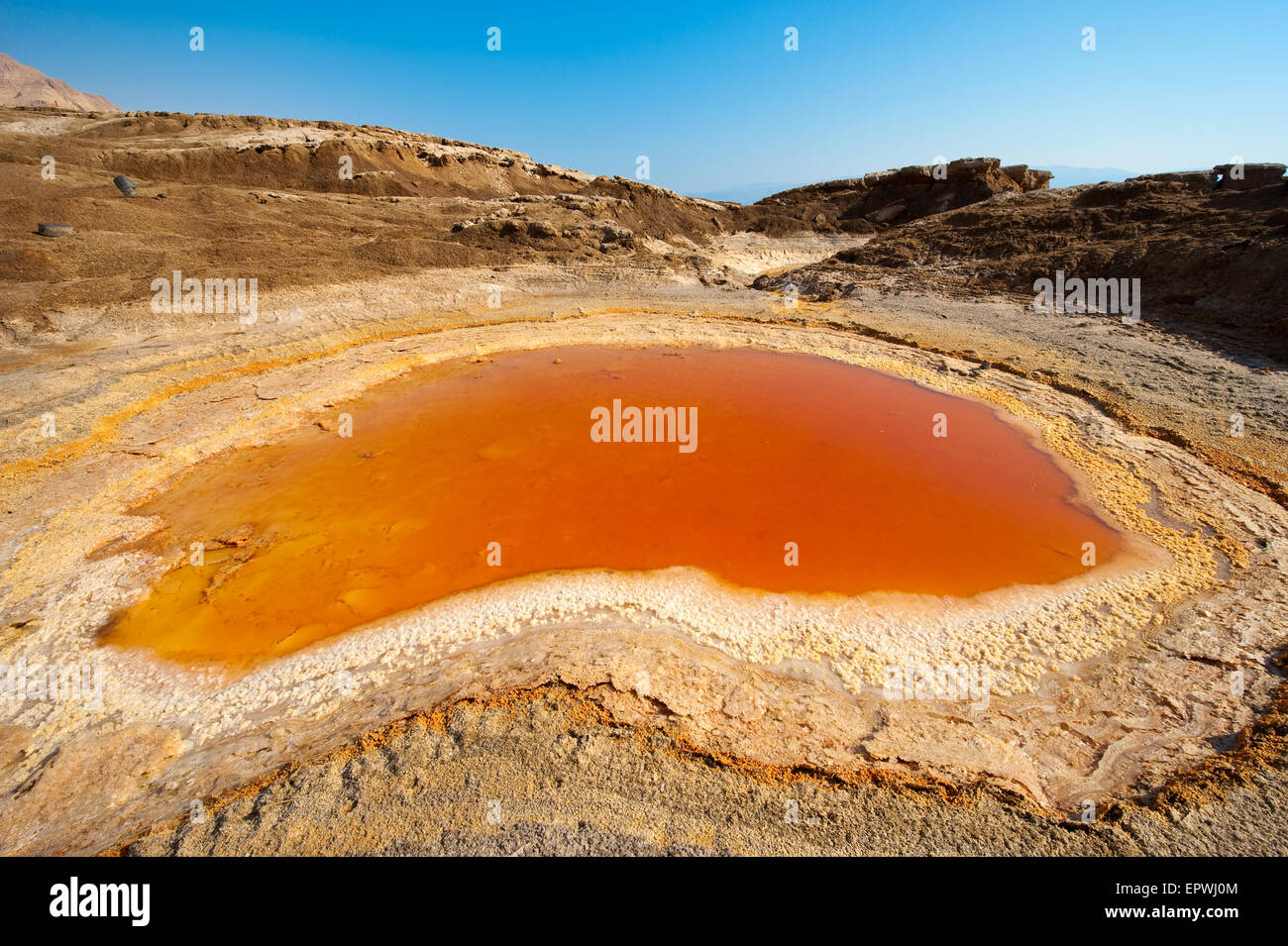 Sinkhole or open pit with orange salty water on the shore's of the dead sea at the end of the summer when the water level is at Stock Photo