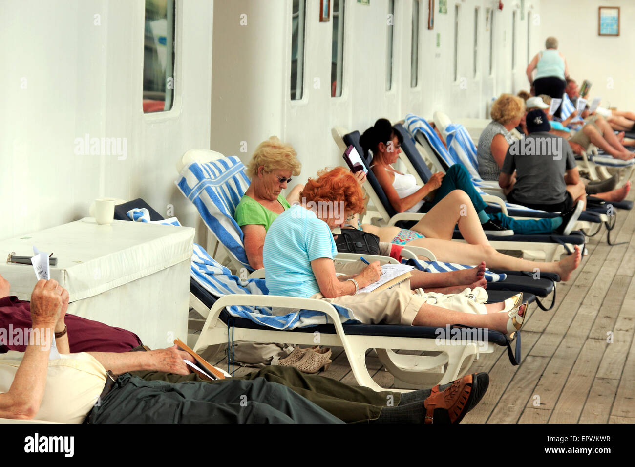 Passengers relaxing on sun loungers on the deck of a cruise ship ...