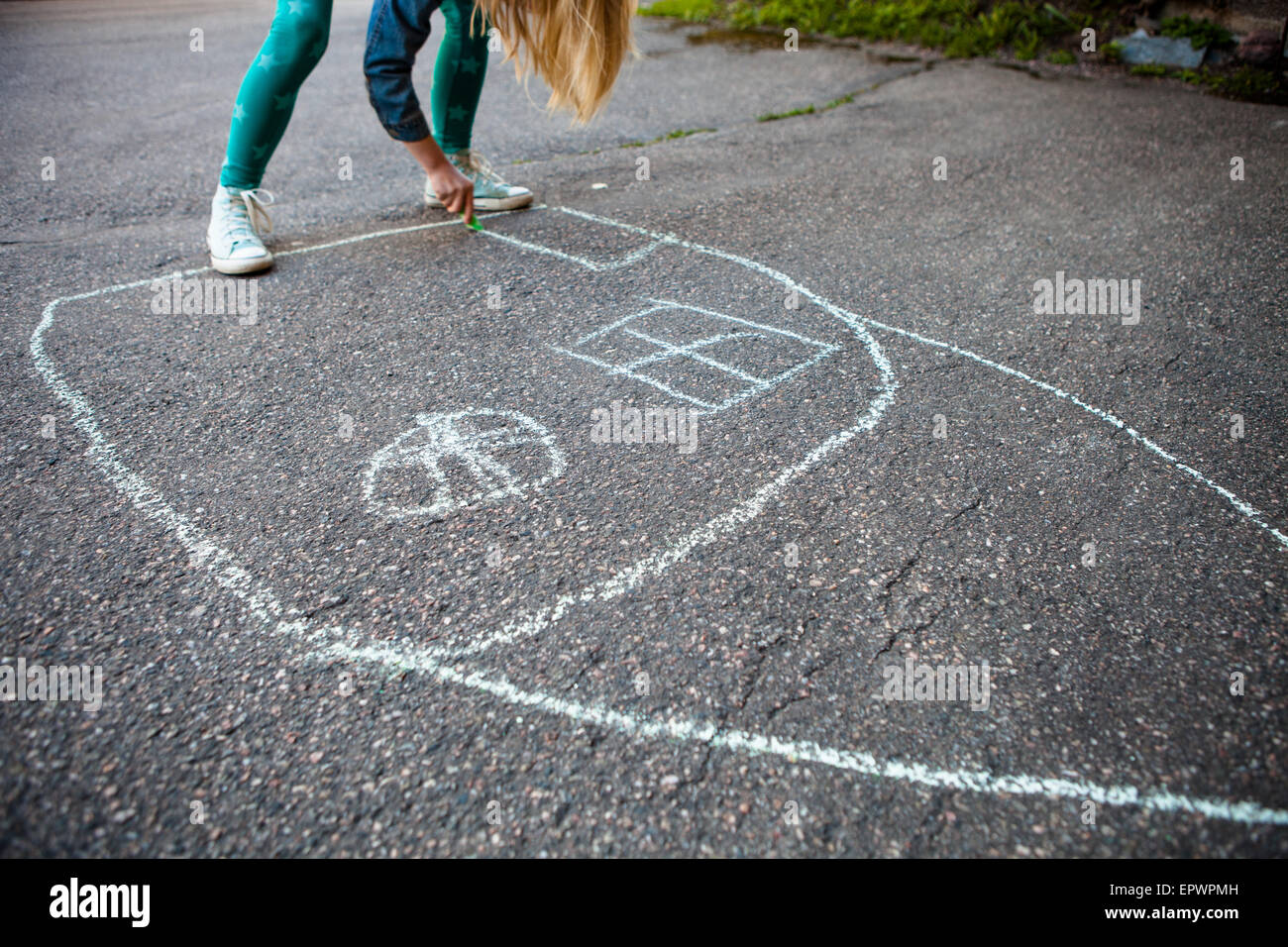 Girl drawing a picture of a house with street chalk outdoors on asphalt Stock Photo