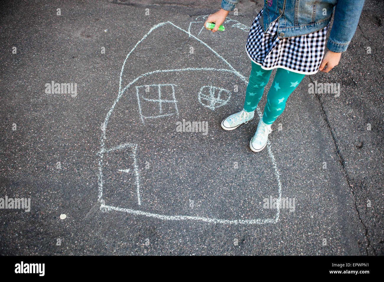 Girl with street chalk outdoors and a drawing of a house on asphalt Stock Photo