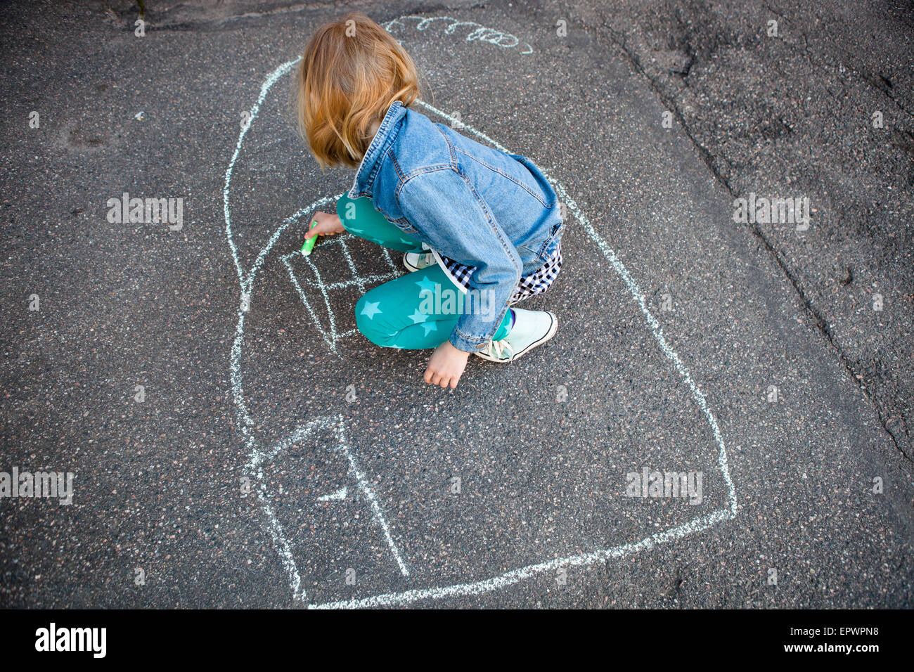 Girl drawing a picture of a house on asphalt with street chalk Stock Photo