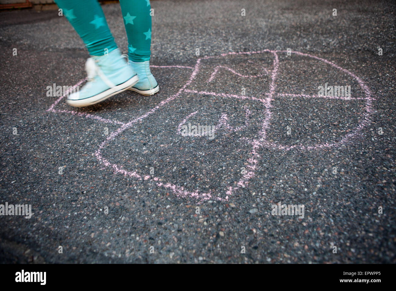 Girl hopping on hopscotch drawn to asphalt with street chalk outdoors Stock Photo