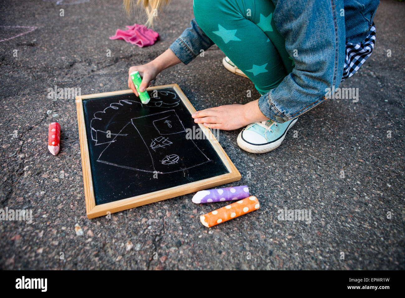 Girl drawing a house on chalkboard outdoors on asphalt with colorful street chalk Stock Photo