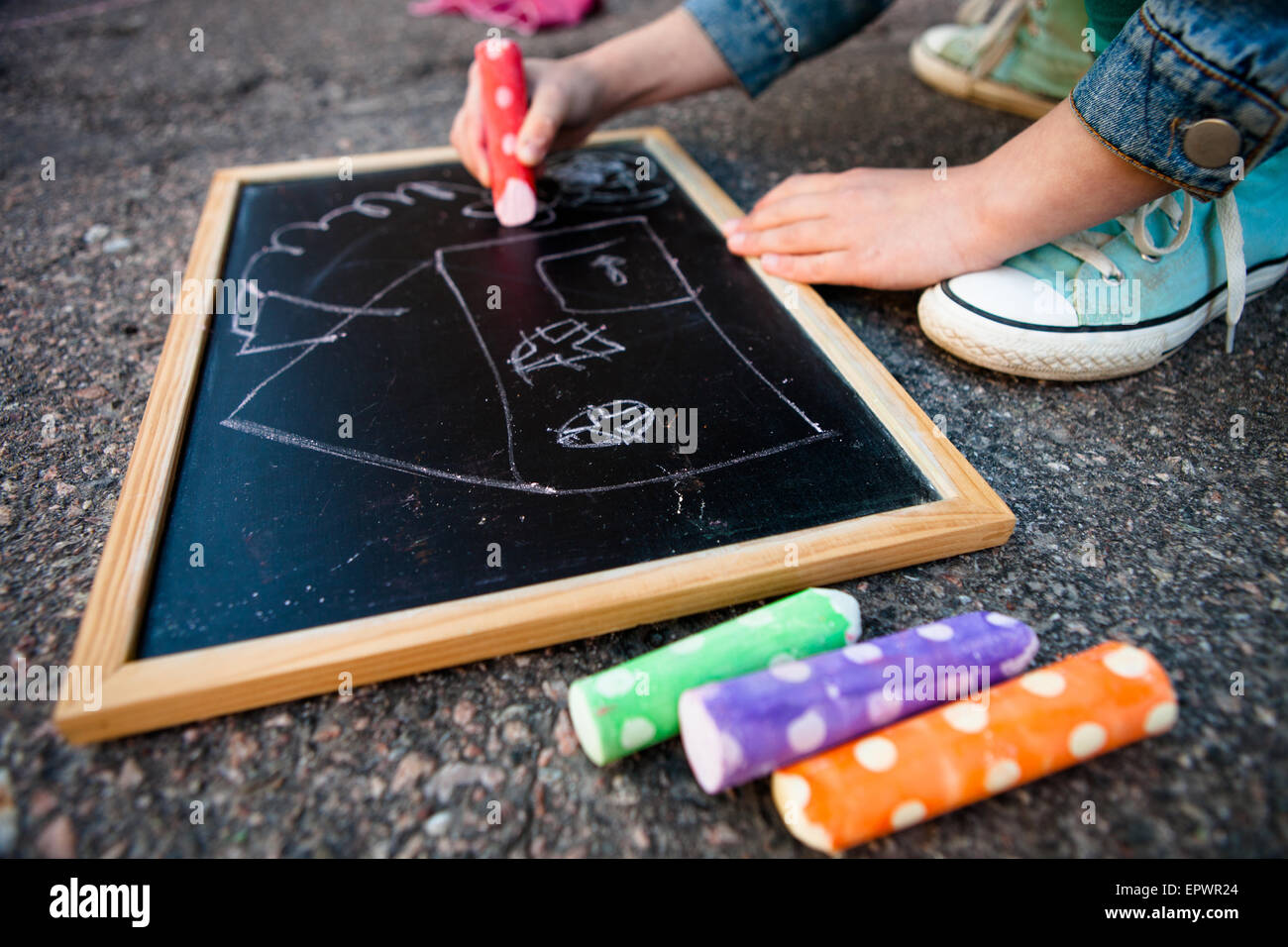 Girl drawing on chalkboard outdoors a picture of a house with colorful street chalk Stock Photo