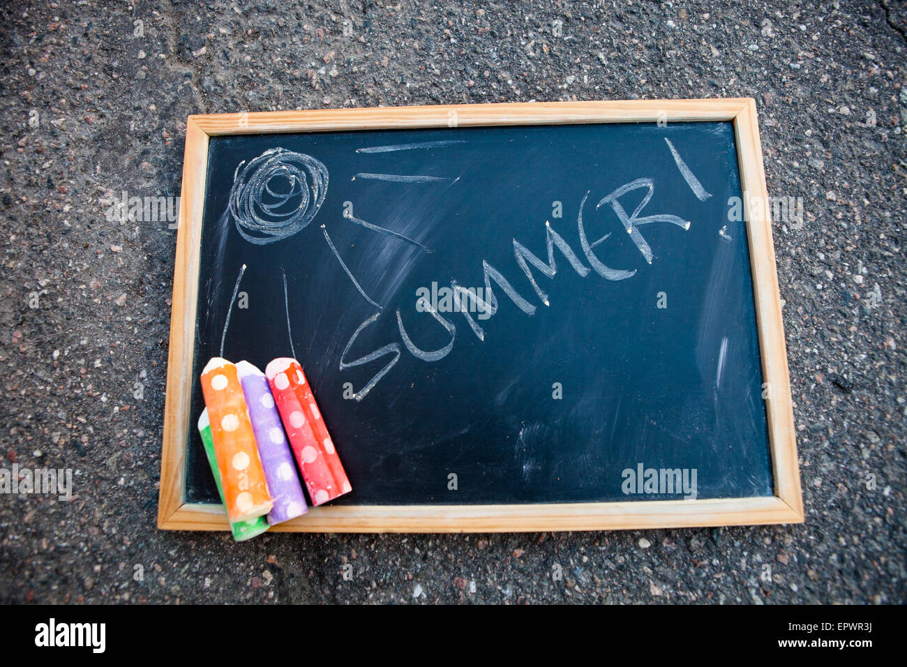 Chalkboard on asphalt that has summer written on it and a sun with colorful street chalk Stock Photo