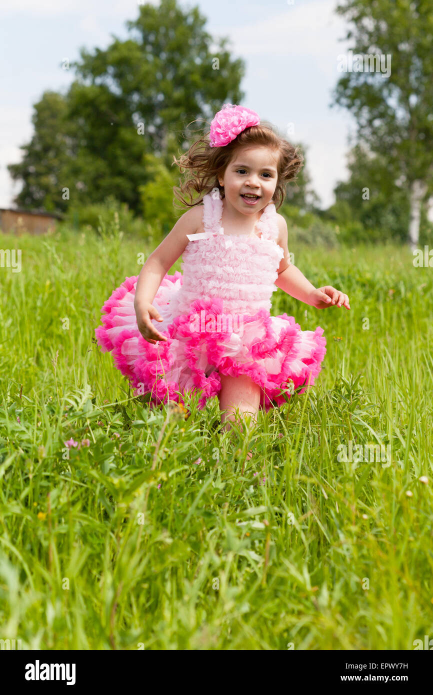 cheerful girl in a pink dress runs on a grass Stock Photo