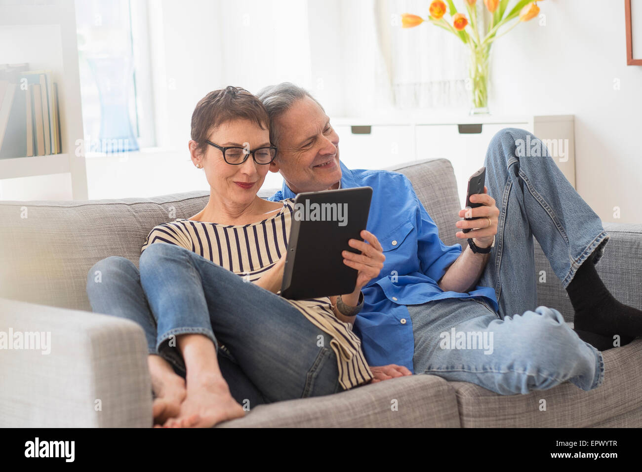 Senior couple sharing electronic devices on sofa Stock Photo