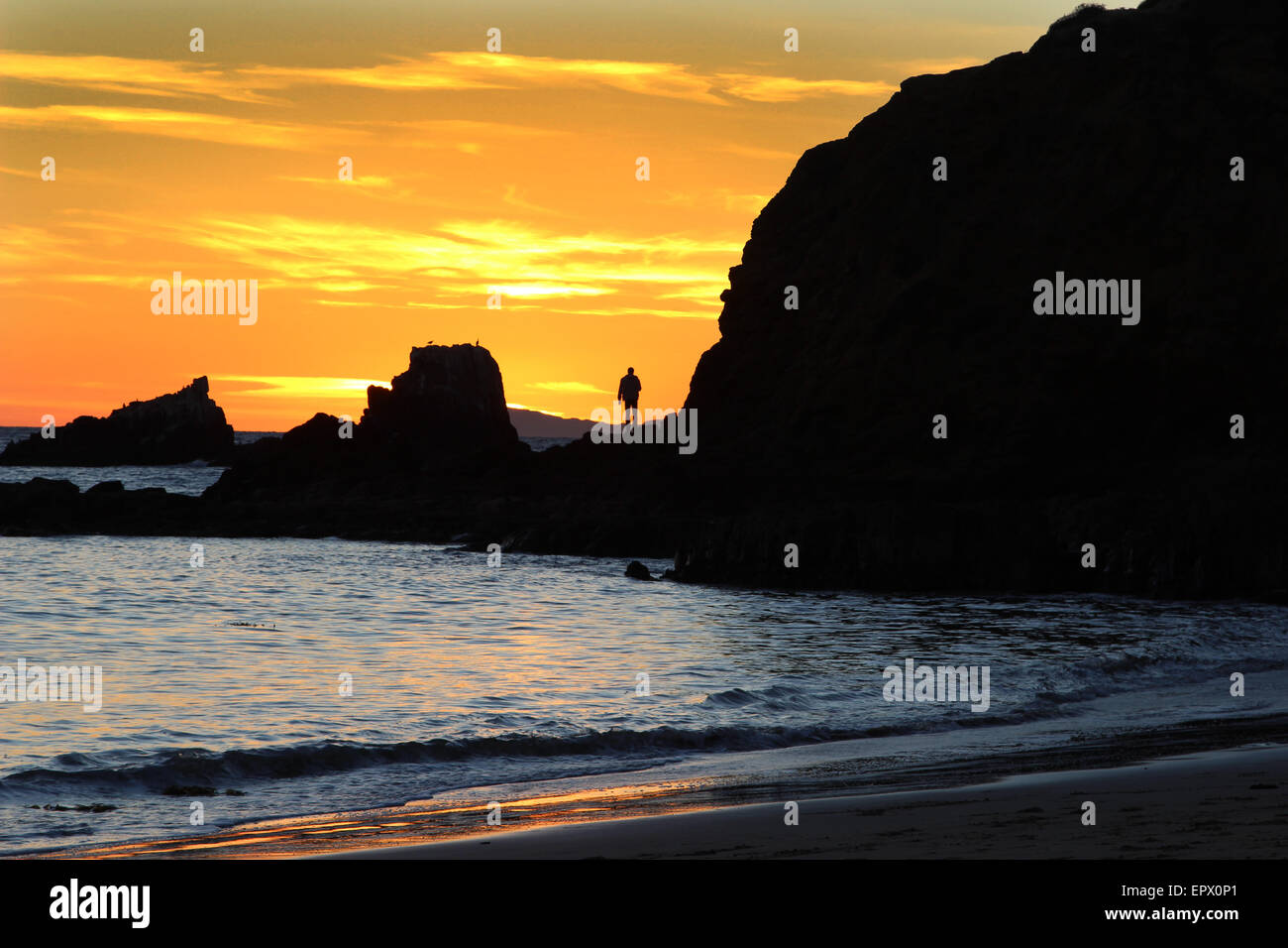 Silhouette of a man at sunset on a rock jetty at Shaw’s Cove in Laguna Beach, Southern California Stock Photo