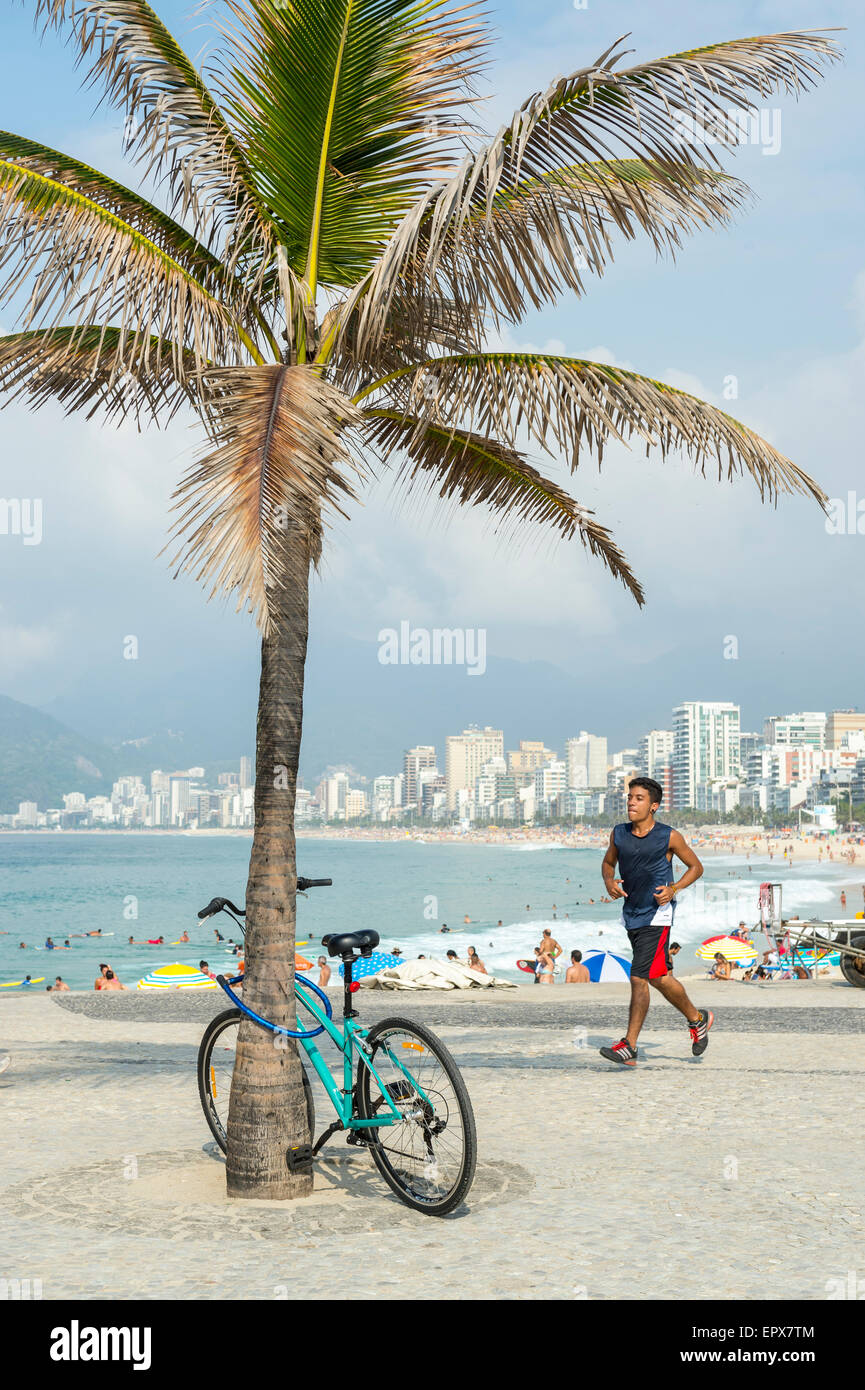 RIO DE JANEIRO, BRAZIL - MARCH 22, 2015: Jogger passes a bicycle locked to a palm tree on the boardwalk at Arpoador near Ipanema Stock Photo
