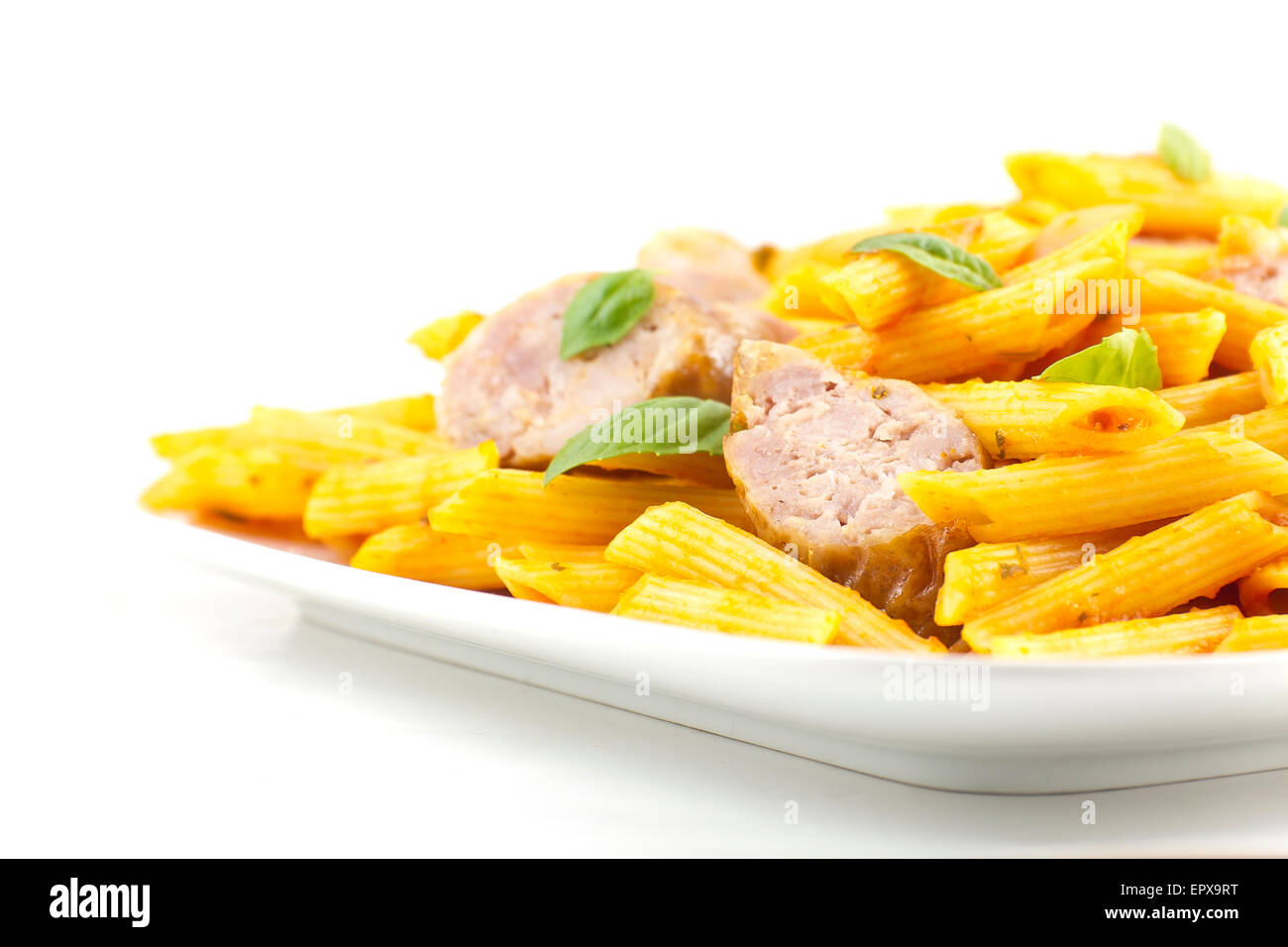 Sliced sausage with penne pasta and red tomato sauce with basil leaves Stock Photo