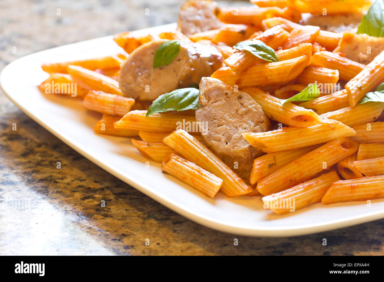 Sliced sausage with penne pasta and red tomato sauce with basil leaves Stock Photo