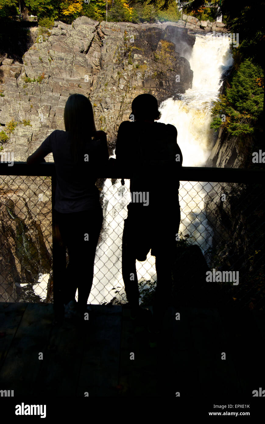 Couple in silhouette at viewpoint looking at raging torrent of water plunging down gorge Canyon Ste Anne River Park Stock Photo