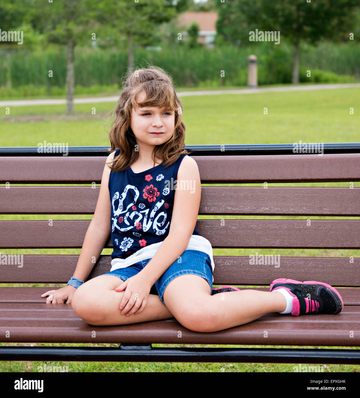 Young girl poses for a portrait while seated on an outdoor park bench Stock Photo