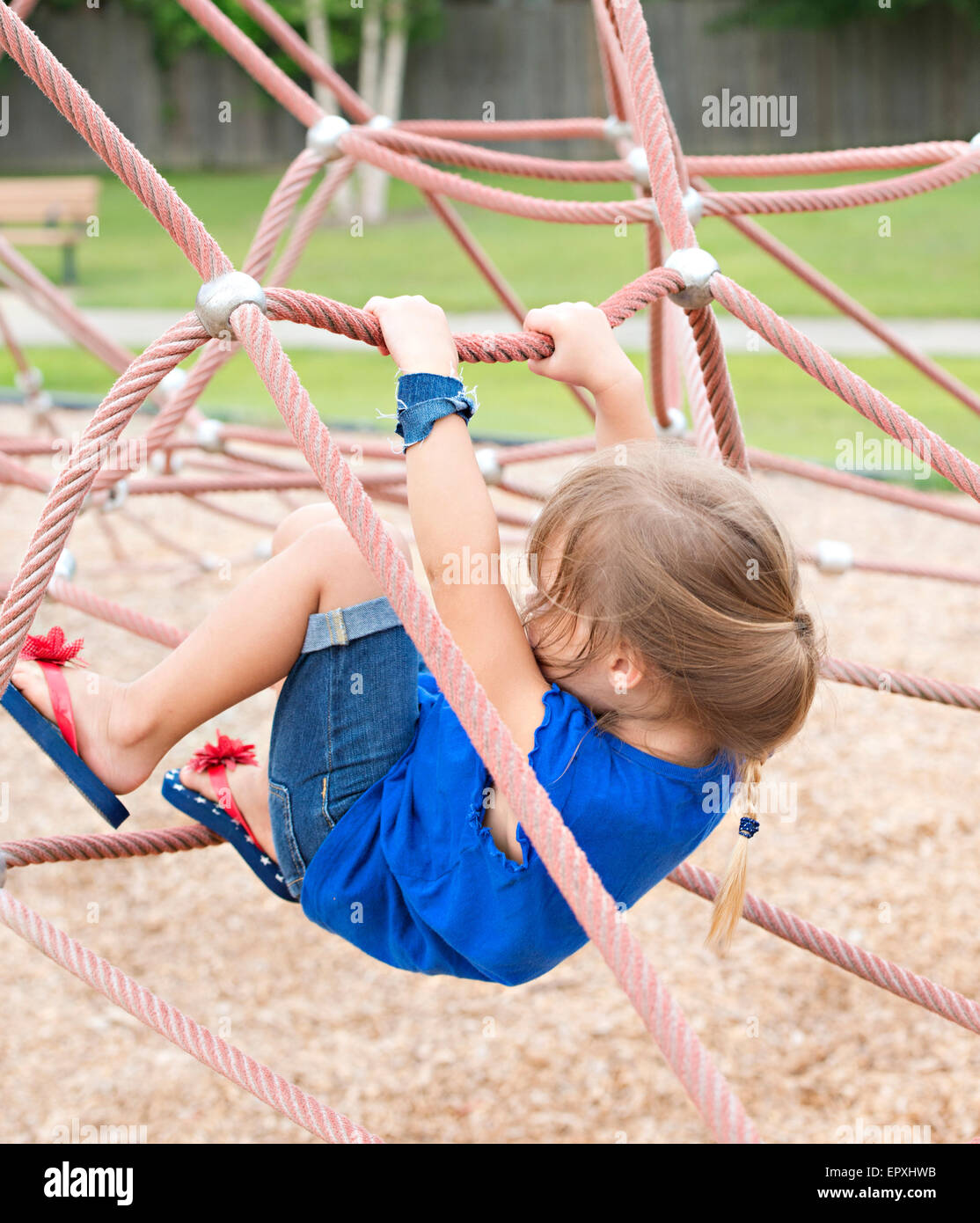 Young girl plays on rope climbing structure at outdoor park playground