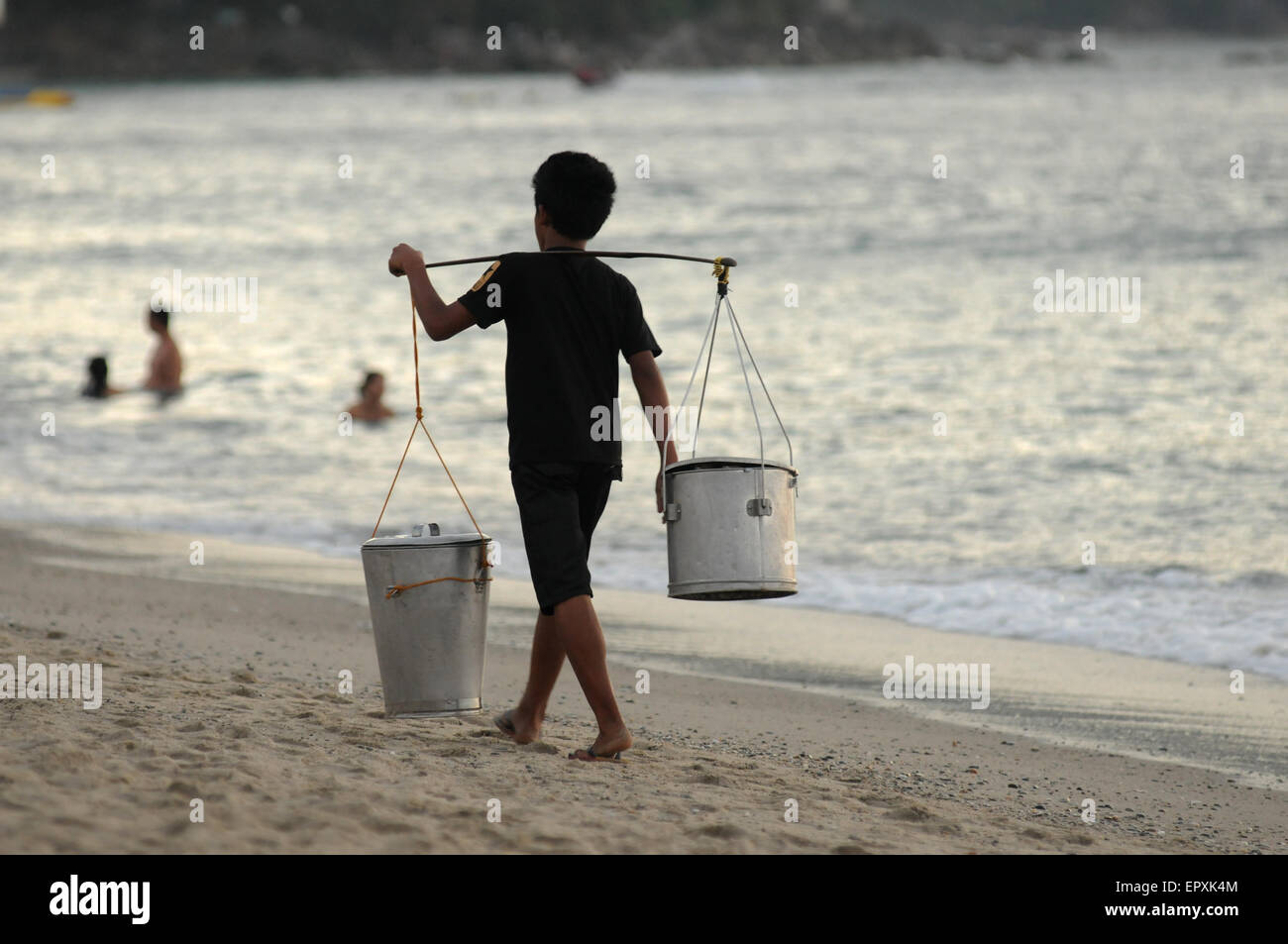 A Filipino balut vendor with two buckets walks along the beach. Mindoro Island, Philippines Stock Photo