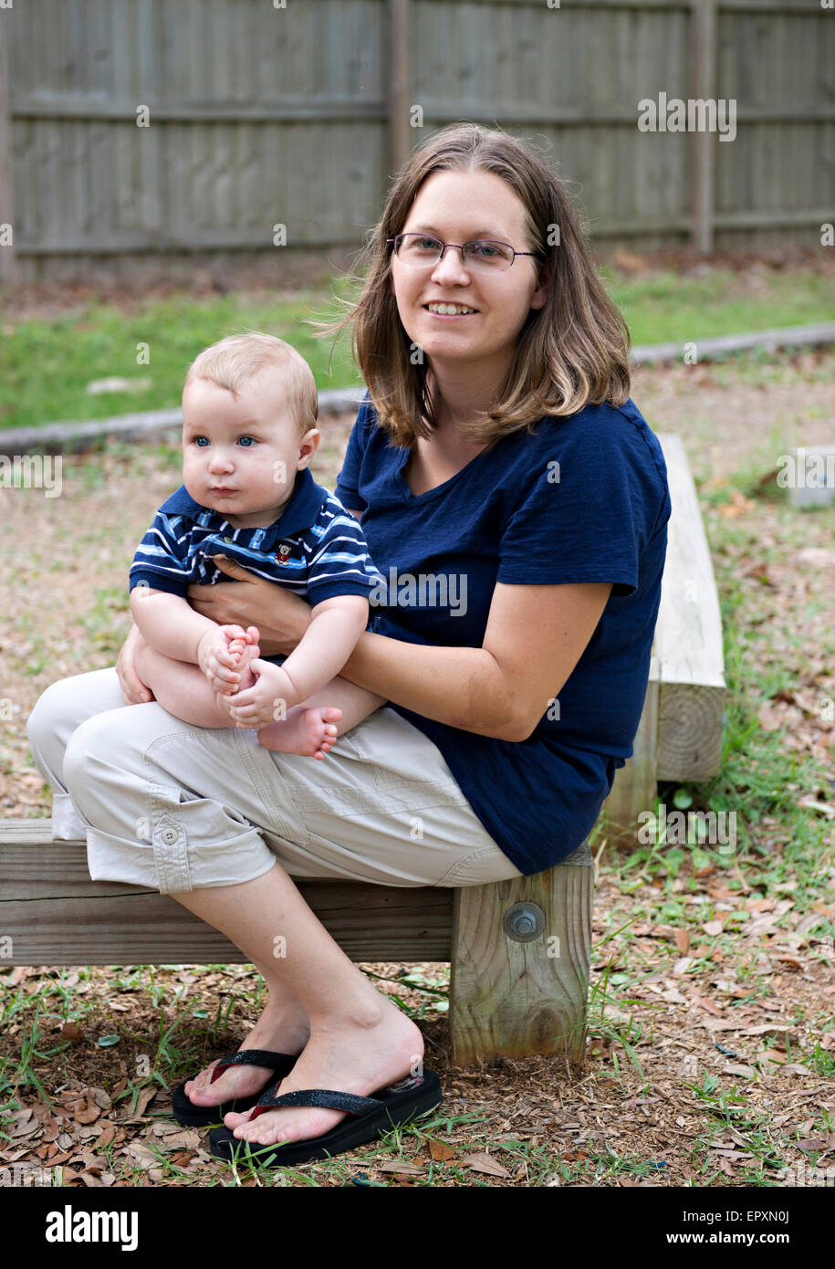 Mother and infant son sit on a wooden balance beam at a park playground Stock Photo