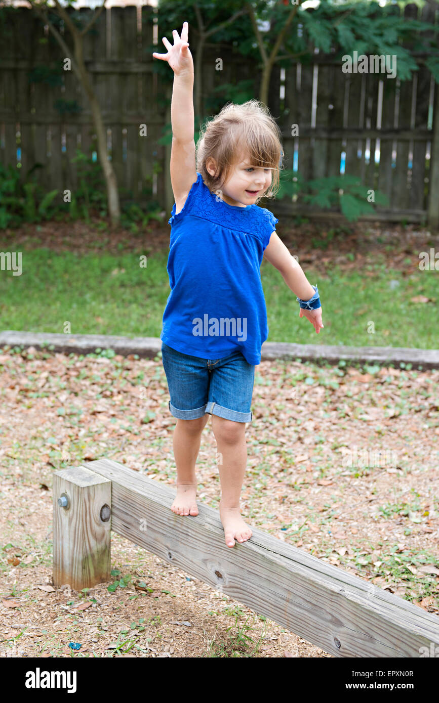 Young girl walks on an outdoor wooden balance beam while posing as a ballerina Stock Photo