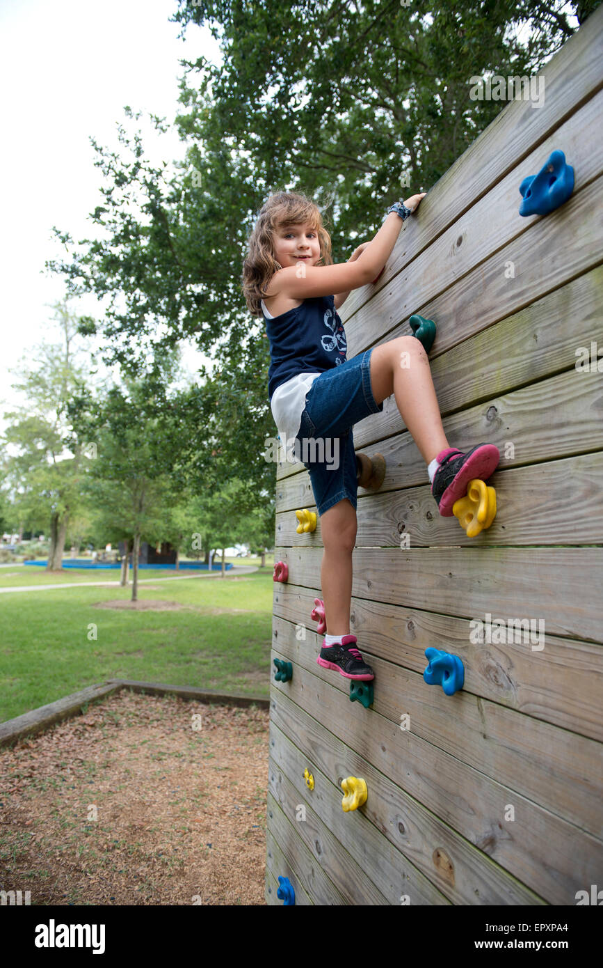 Young girl climbs a rock wall in an outdoor playground park Stock Photo