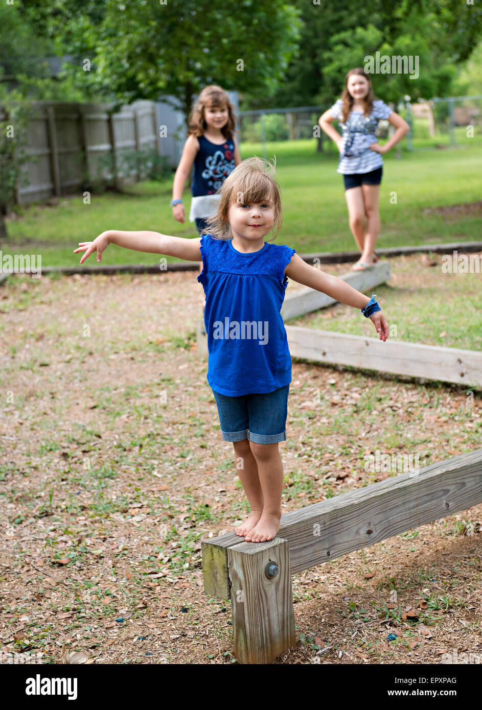 Sibling sisters walk along an outdoor wooden balance beam at a park playground Stock Photo