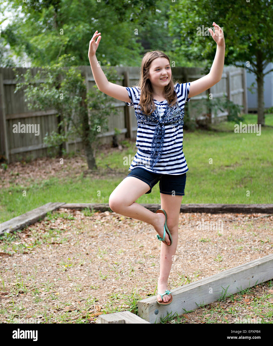 Teenage girl walking on an outdoor wooden balance beam with a ballerina pose Stock Photo