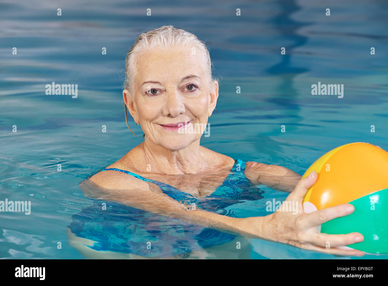 Happy senior woman with water ball in swimming pool doing aqua fitness Stock Photo