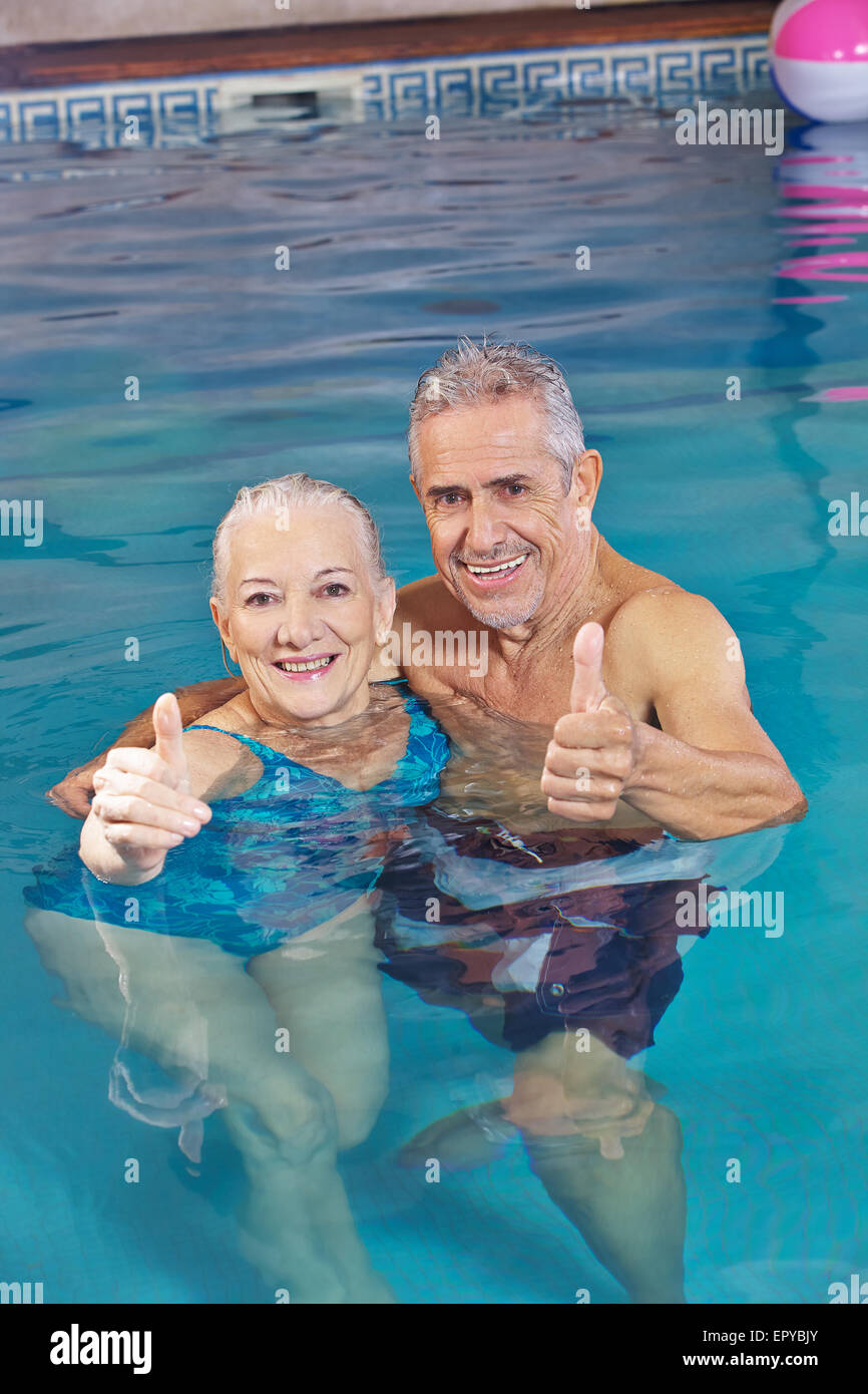 Happy senior couple bathing in swimming pool holding their thumbs up Stock Photo
