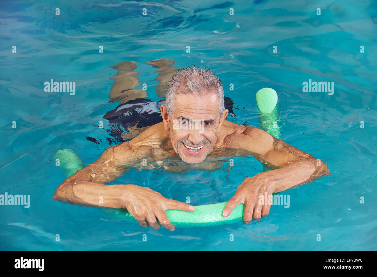 Old man swimming in water of hotel pool with swim noodle Stock Photo