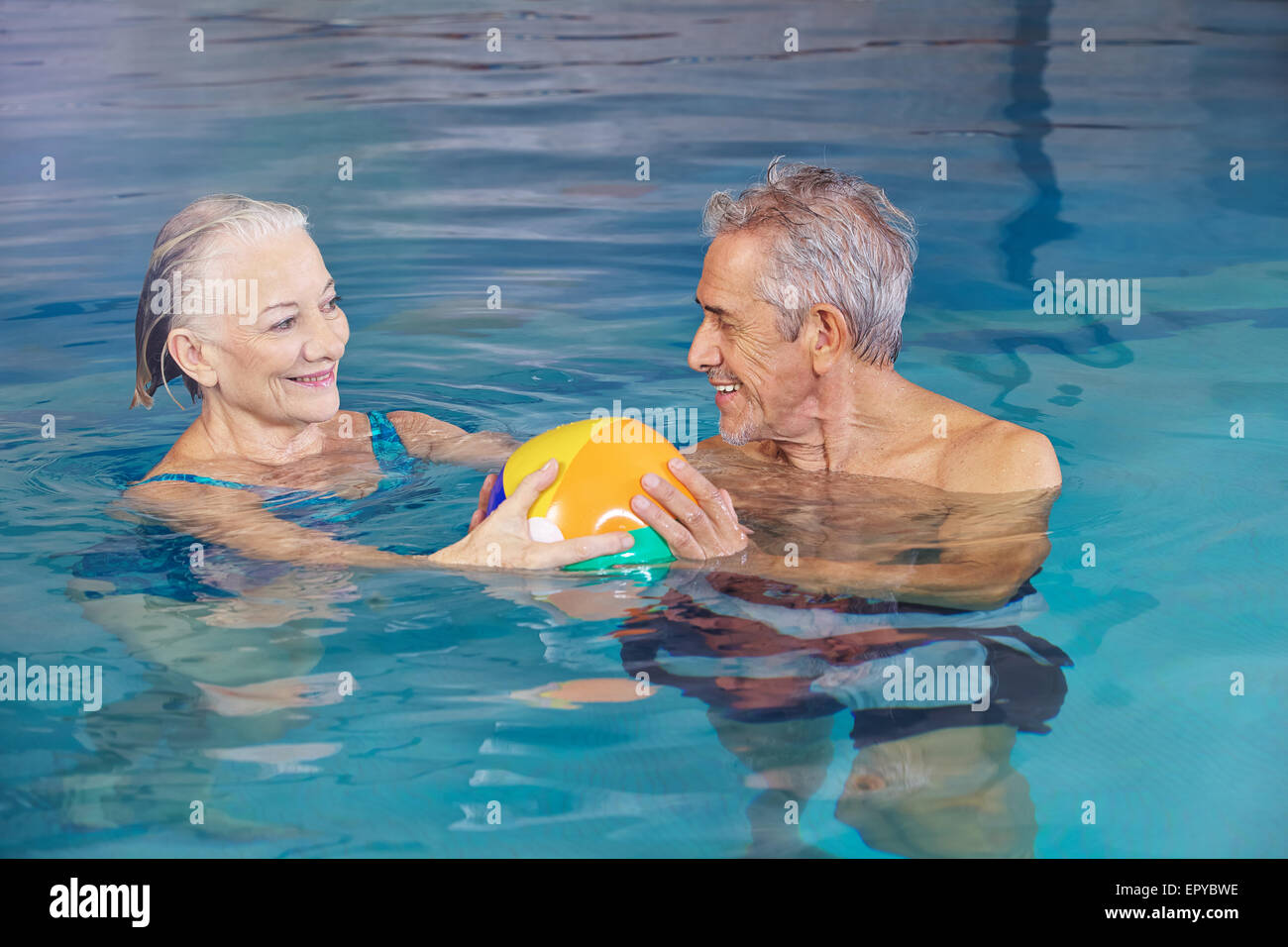 Happy senior couple playing water ball with beach ball in swimming pool Stock Photo