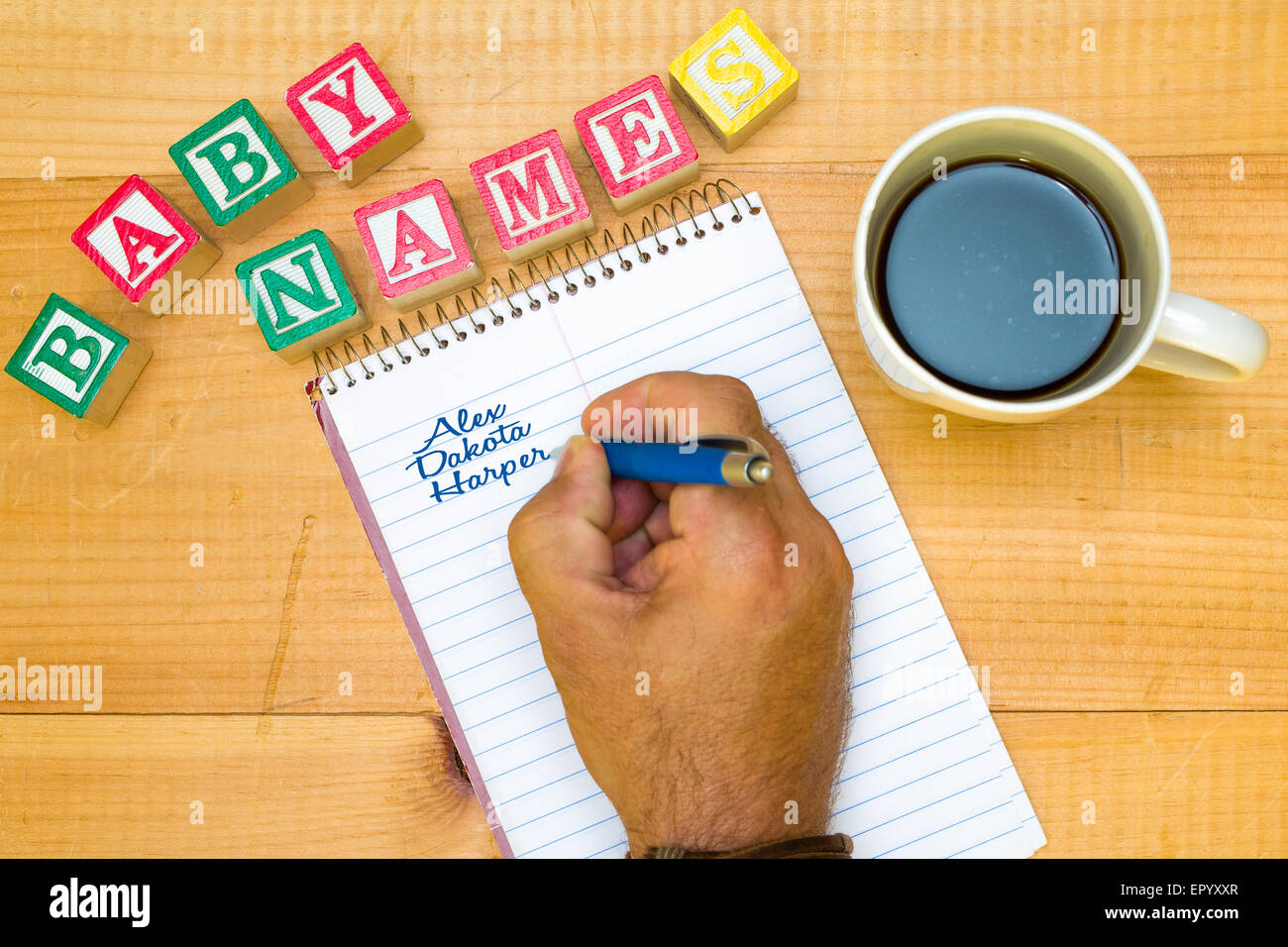 Hand writing out potential baby names on a notepad with a coffee. Stock Photo