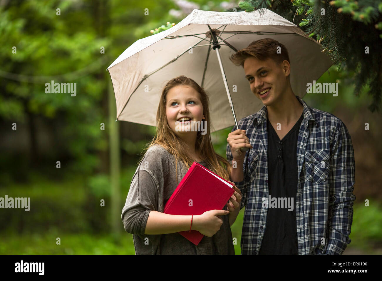 Young couple in the Park under an umbrella, a girl holds a red book in his hands. Stock Photo