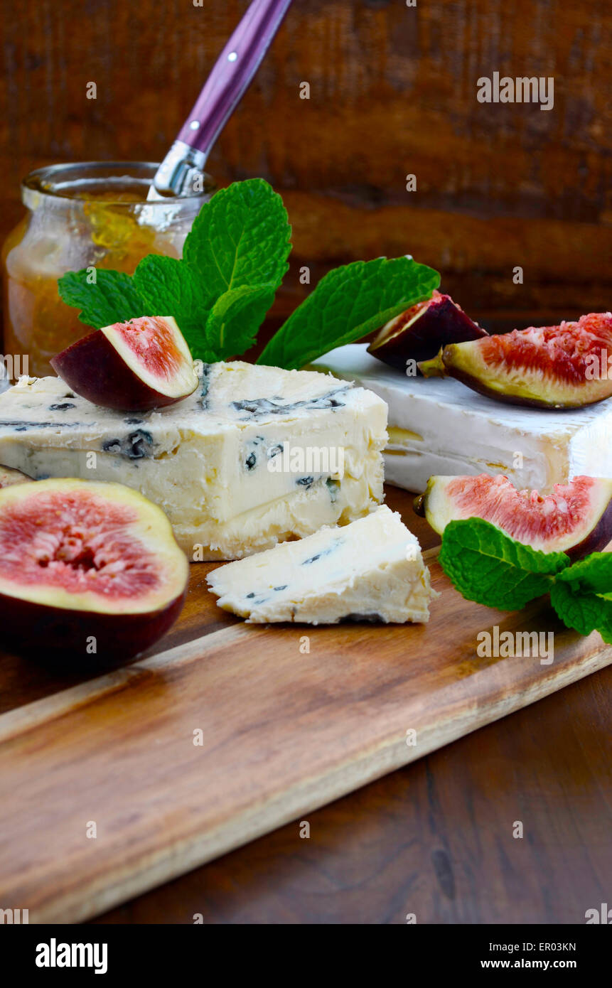 Fresh figs on wooden cutting chopping board with jar of fig jelly preserve and gourmet cheese on dark wood rustic table backgrou Stock Photo