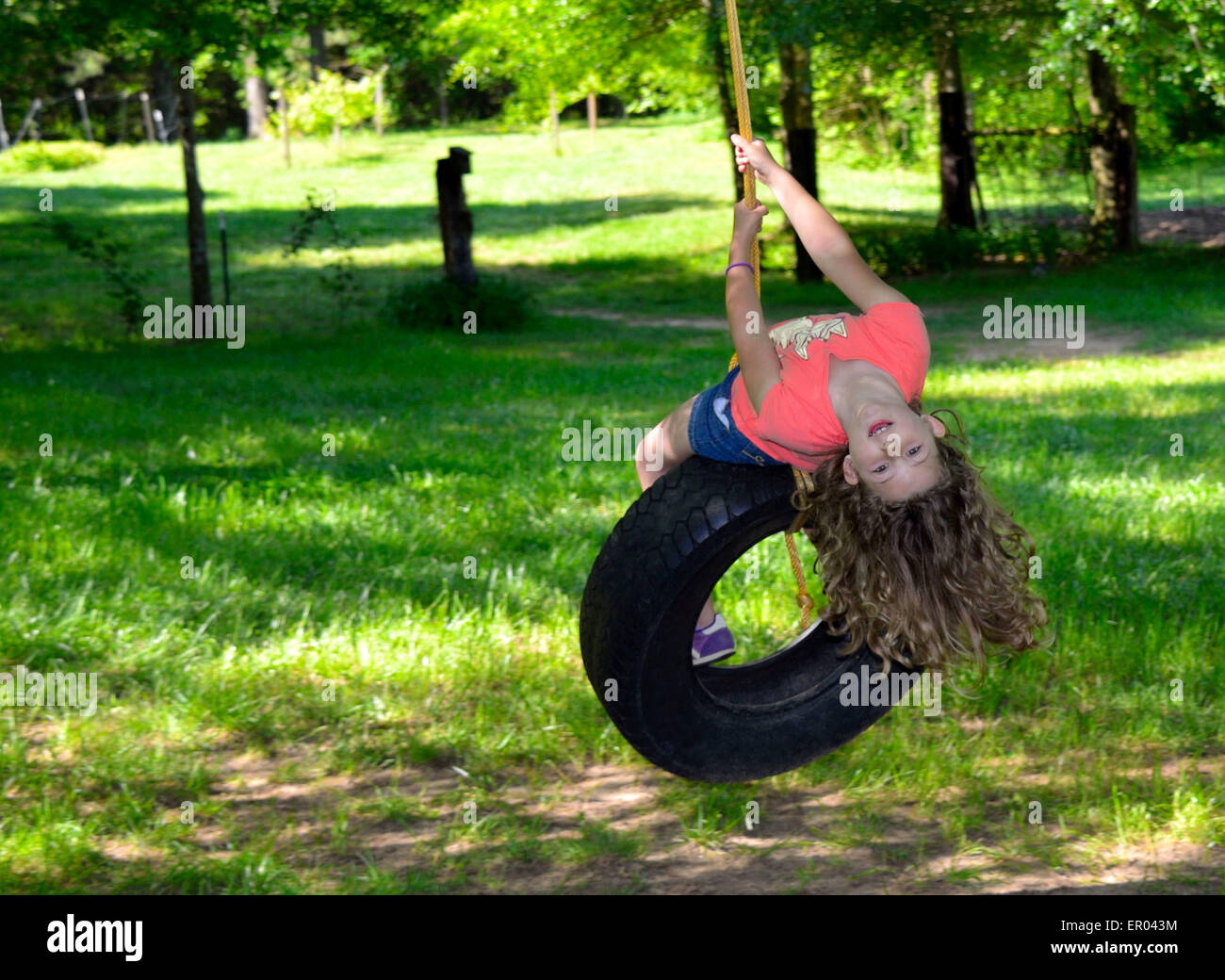 Young elementary aged girl swinging on a tire swing in the bright spring sunshine Stock Photo