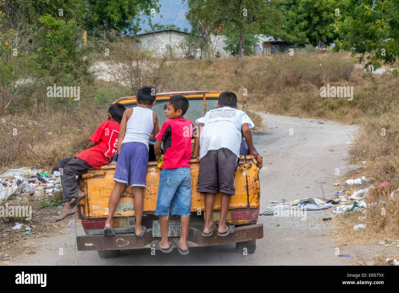 Boys riding on the back of a pickup truck hauling items from a garbage