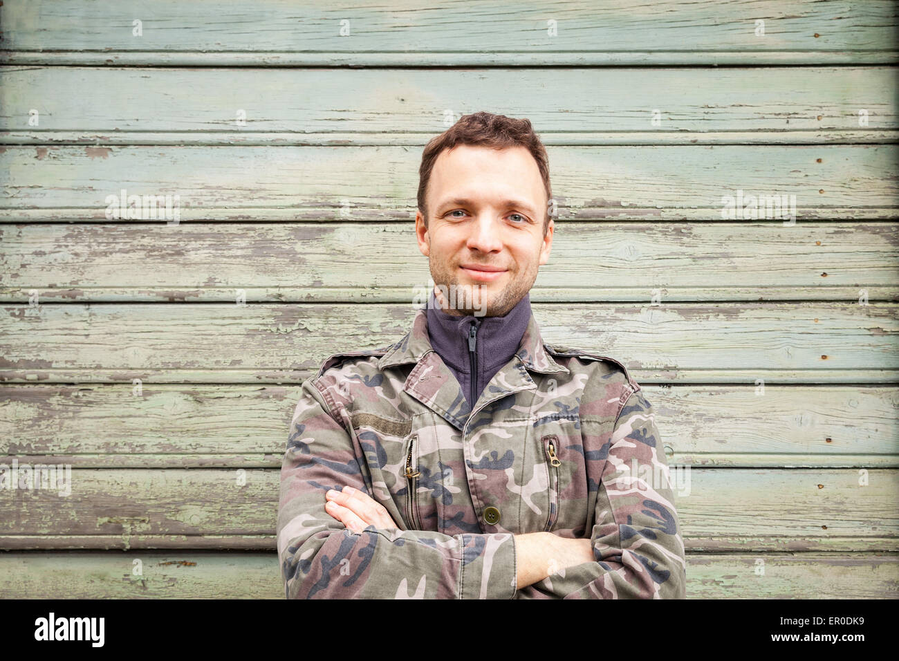 Young smiling Caucasian man in camouflage, outdoor portrait over green ...