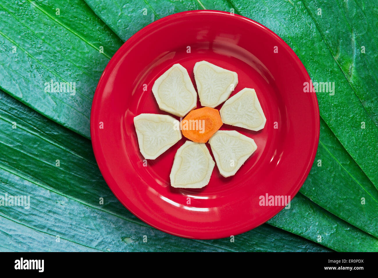 Slices of parsley and carrot arranged in a flower shape, served on red ceramic plate. Diet concept. Organic food. Stock Photo
