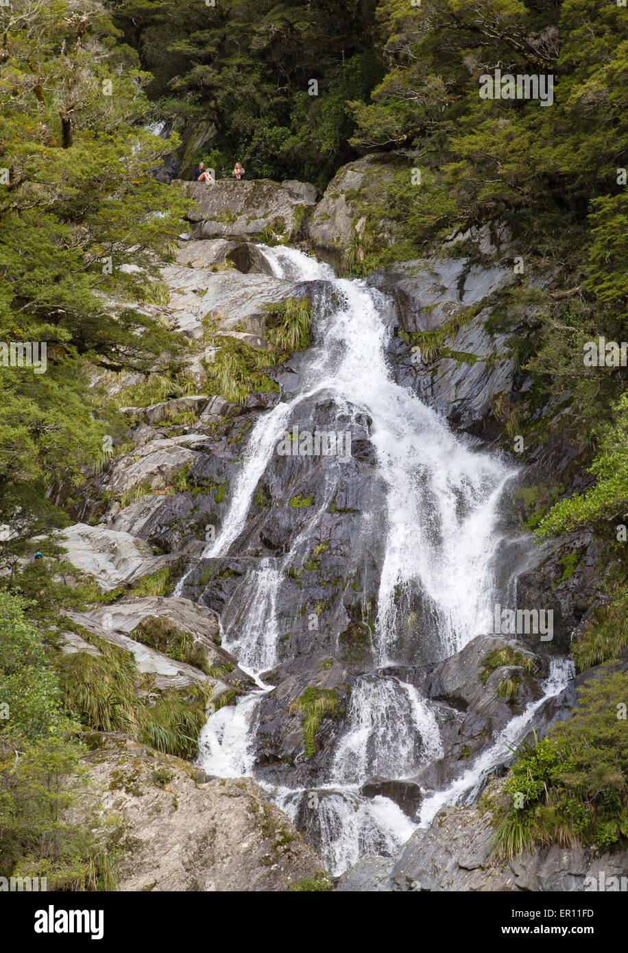 Two young women sitting at the head of Fantail Falls  Mount Aspiring National Park near Haast Highway South Island New Zealand. Stock Photo