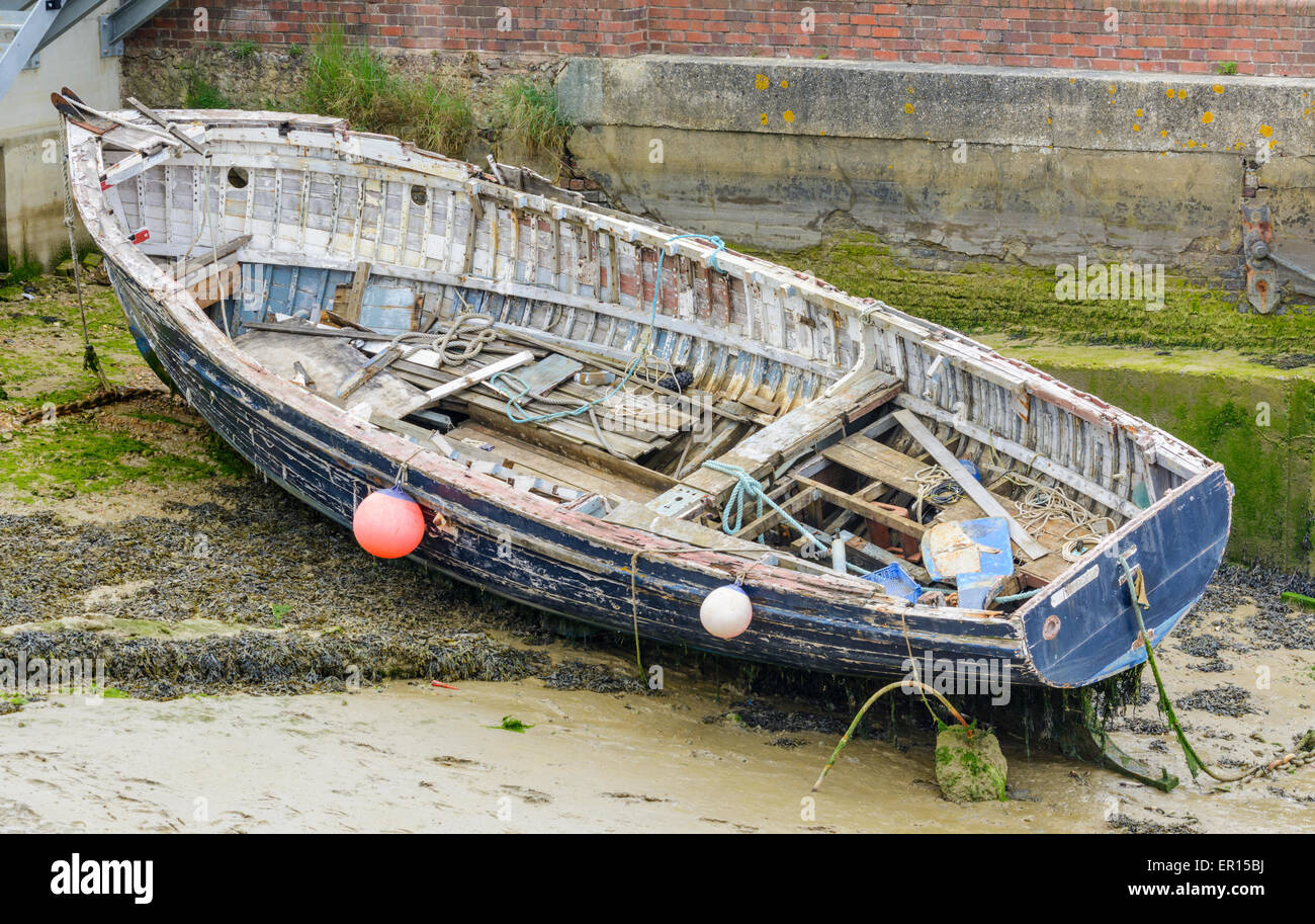 A large wooden rowing boat on the mud at the side of the river, at low tide. Stock Photo
