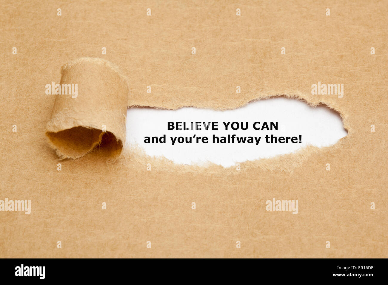 The text Believe you can and you're halfway there, appearing behind torn brown paper. Stock Photo