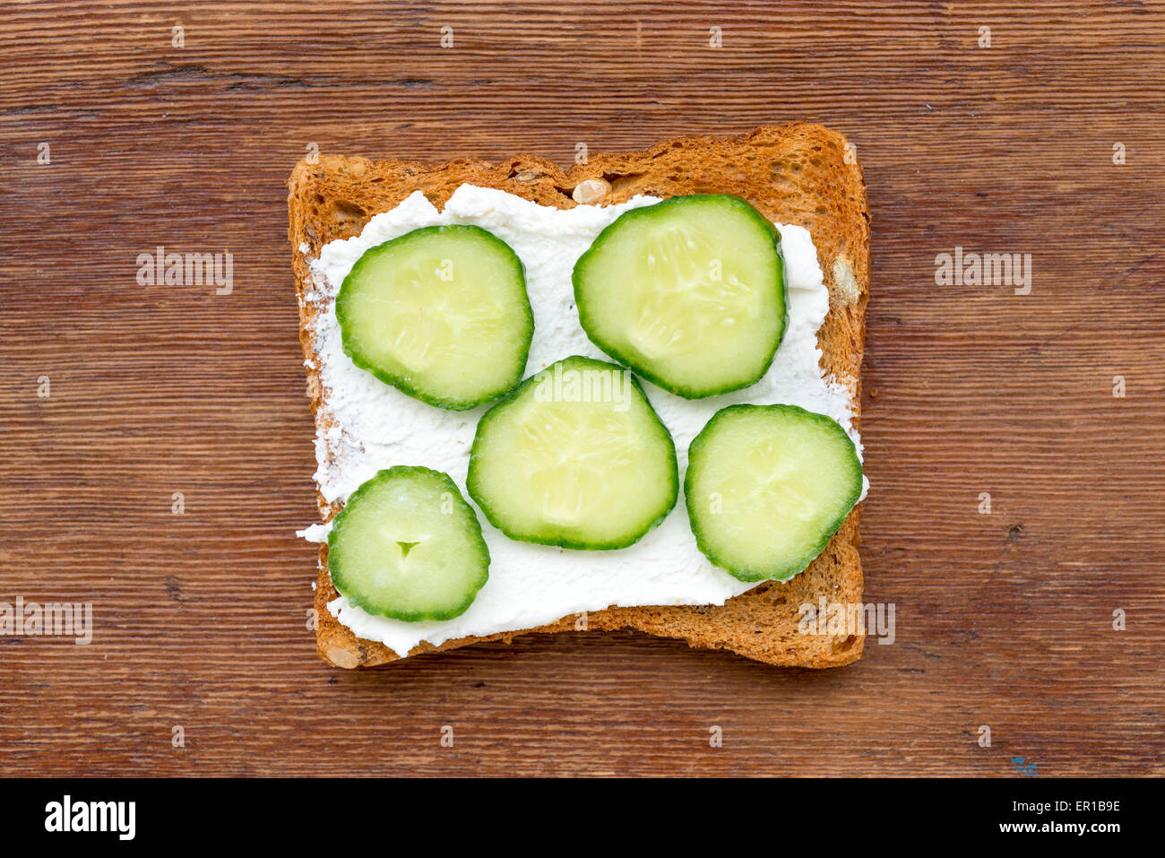fried toast with soft cheese and cucumber slices on vintage wood Stock