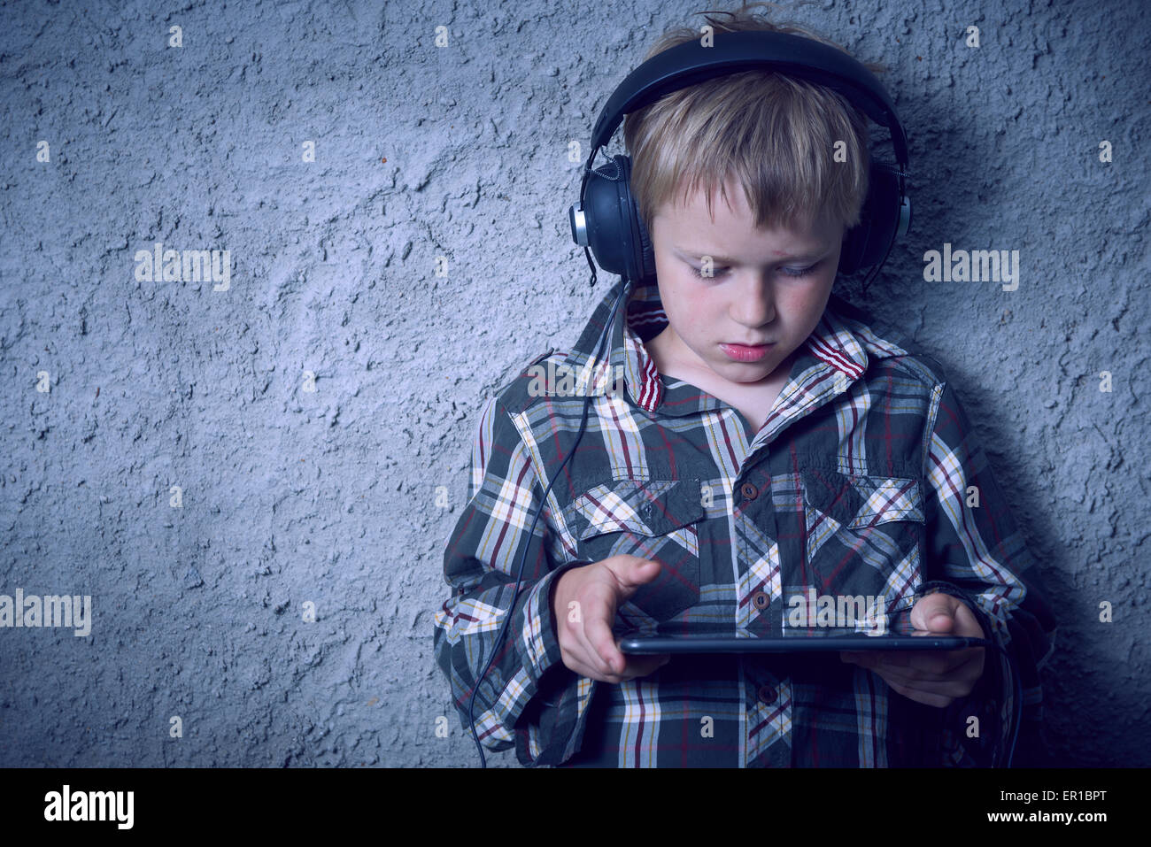 Child blond Boy listening to music with headphones and using digital tablet Stock Photo