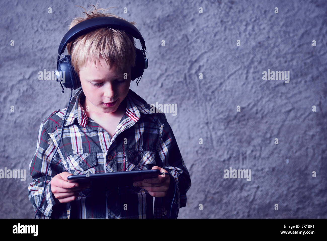 Child blond Boy listening to music with headphones and using digital tablet Stock Photo