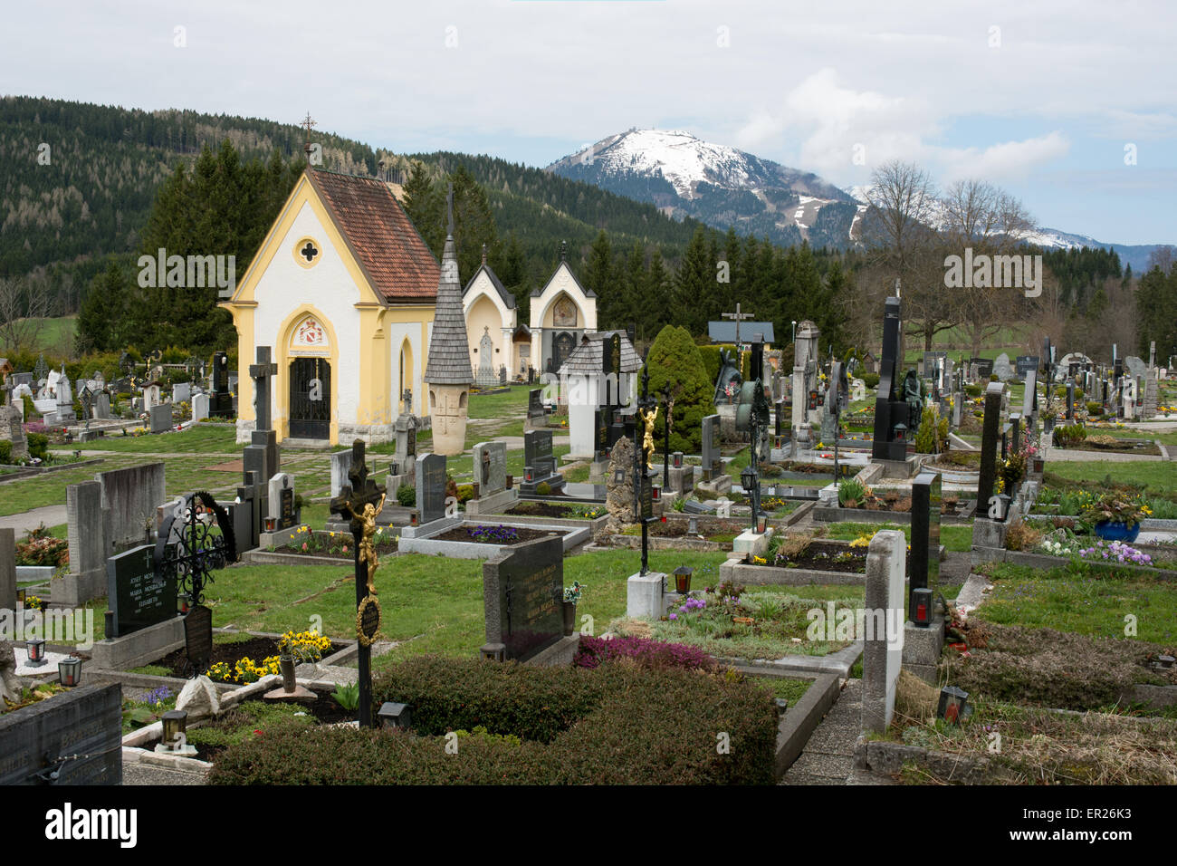 A peaceful and well maintained graveyard in the hill top town of Mariazell in Austria. Snow is still on the mountains in May Stock Photo