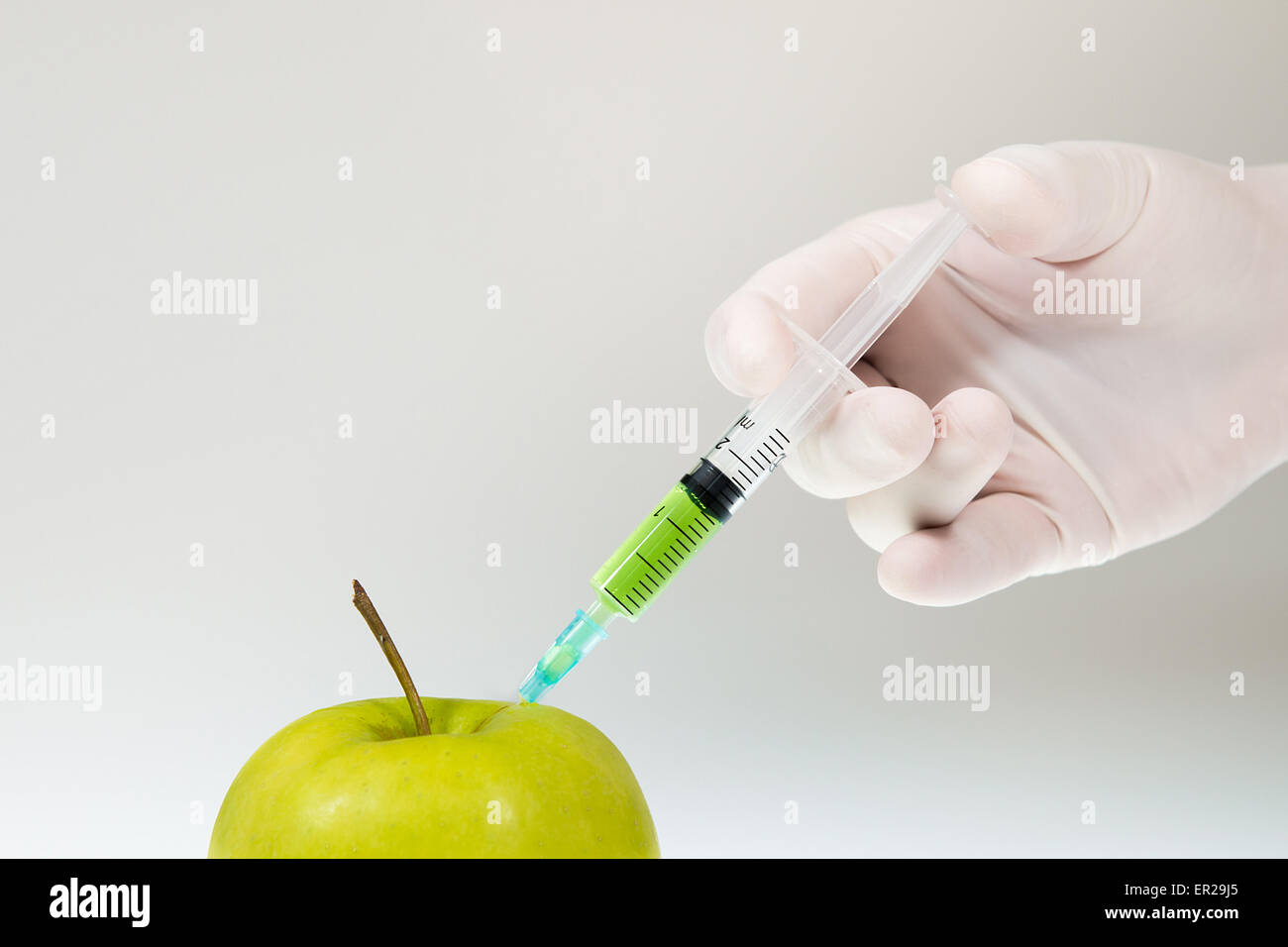 Hand is injecting chemicals into an apple. White and grey gradient background. High res photo taken with a full frame Nikon D610 Stock Photo