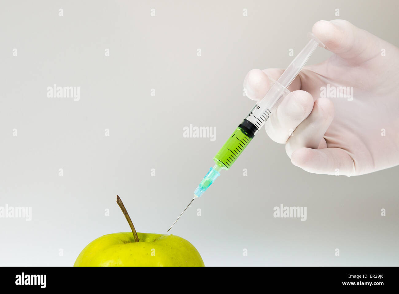 Hand is injecting chemicals into an apple. White and grey gradient background. High res photo taken with a full frame Nikon D610 Stock Photo